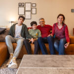 Father’s search for diagnosis leads to innovative AI breakthrough A family of four at home sit on a sofa looking at the camera.