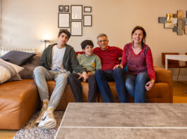 Father’s search for diagnosis leads to innovative AI breakthrough A family of four at home sit on a sofa looking at the camera.