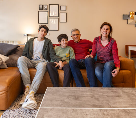Father’s search for diagnosis leads to innovative AI breakthrough A family of four at home sit on a sofa looking at the camera.