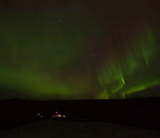 NASA Plans Triple Rocket Launch from Alaska for Aurora Study A time-lapse of auroral activity looks like green, red, yellow, and orange curtains traveling across a clear night sky filled with stars. In the dark land below, faraway launch pads are lit by floodlights, and two tiny vertical rockets can be seen waiting for launch.