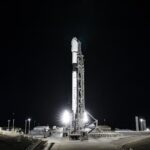 NASA, Europe Ready to Launch Sentinel-6B Earth Satellite A wide-angle, distant photo of a white rocket on the launch pad, brightly lit, with a black night sky behind it.