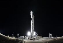NASA, Europe Ready to Launch Sentinel-6B Earth Satellite A wide-angle, distant photo of a white rocket on the launch pad, brightly lit, with a black night sky behind it.