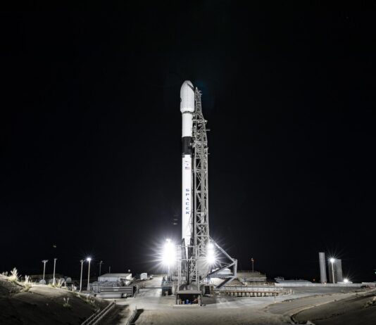 NASA, Europe Ready to Launch Sentinel-6B Earth Satellite A wide-angle, distant photo of a white rocket on the launch pad, brightly lit, with a black night sky behind it.