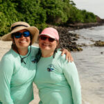Interview: OCEANOS Instructor María Fernanda Barbarena-Arias – NASA Two Puerto Rican women stand on a beach, both wearing teal longsleeve shirts and sunglasses. The one on the left has a tan, wide-brimmed hat, and the one on the right has a pink baseball cap.