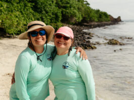 Discussion with NASA’s OCEANOS Expert María Fernanda Barbarena-Arias Two Puerto Rican women stand on a beach, both wearing teal longsleeve shirts and sunglasses. The one on the left has a tan, wide-brimmed hat, and the one on the right has a pink baseball cap.