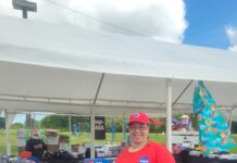 Tina Preyan Drives Innovation at NASA’s Johnson Space Center Johnson Space Center Food Services Specialist Tina Preyan stands in front of a NASA Store table at an outdoor event.