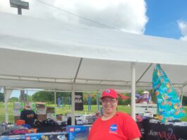 Tina Preyan Drives Innovation at NASA’s Johnson Space Center Johnson Space Center Food Services Specialist Tina Preyan stands in front of a NASA Store table at an outdoor event.