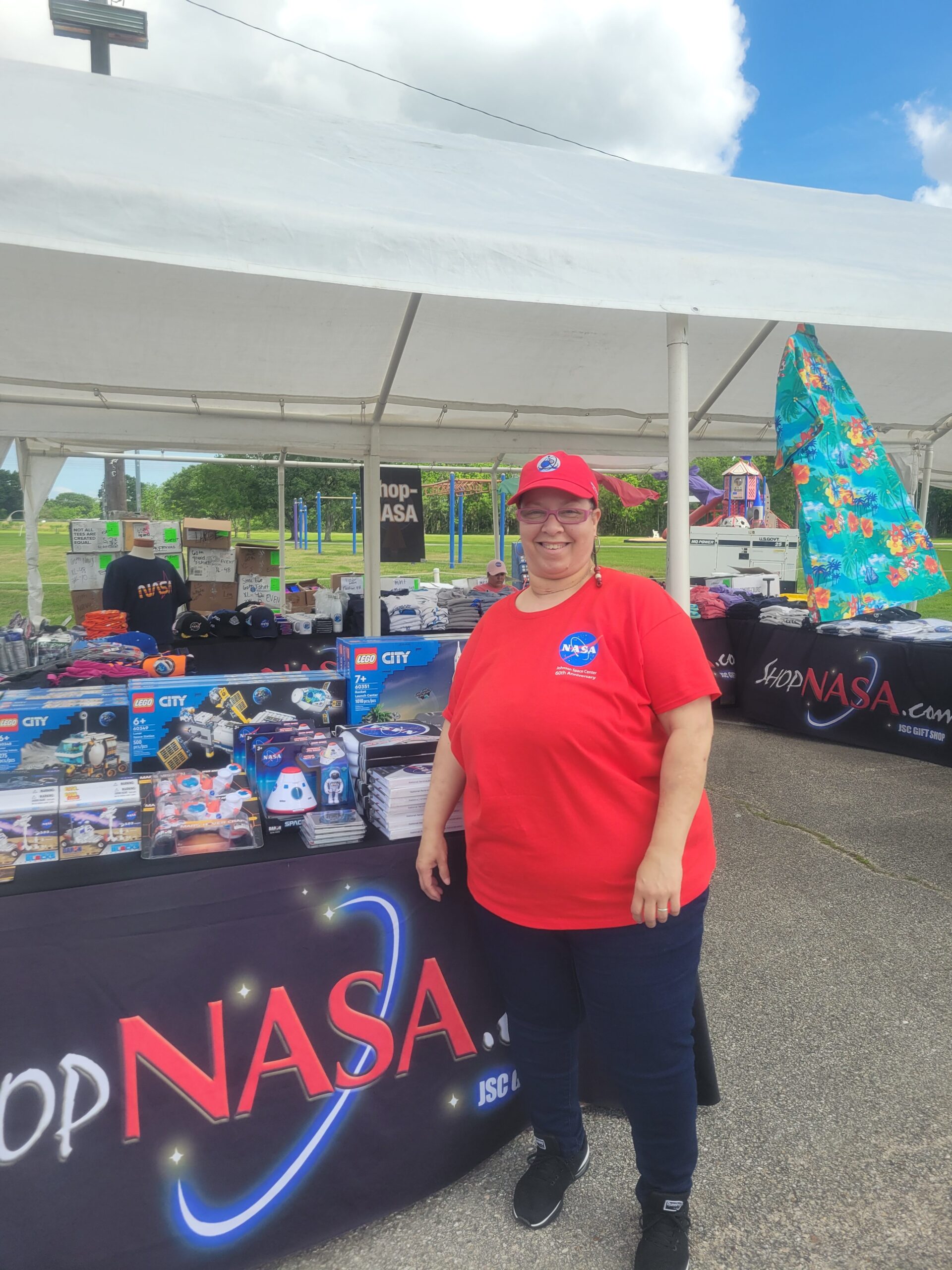 20220428 163053 rotated.jpg Johnson Space Center Food Services Specialist Tina Preyan stands in front of a NASA Store table at an outdoor event.