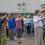 Urban Parks Link Communities to Space Science through NASA Training A group of people stand outside holding white Styrofoam balls on a stick with arms outstretched to model moon phases.