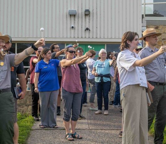 Urban Parks Link Communities to Space Science through NASA Training A group of people stand outside holding white Styrofoam balls on a stick with arms outstretched to model moon phases.