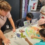 NASA’s Crayon Initiative Fuels Earth and Sky Discoveries People gather around a pixelated poster of the Moon’s far side and color in the small boxes with a crayon color that corresponds to the elevation in that area.