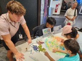 NASA’s Crayon Initiative Fuels Earth and Sky Discoveries People gather around a pixelated poster of the Moon’s far side and color in the small boxes with a crayon color that corresponds to the elevation in that area.