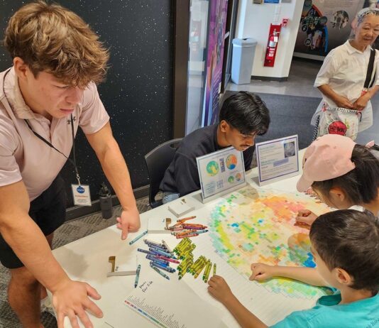NASA’s Crayon Initiative Fuels Earth and Sky Discoveries People gather around a pixelated poster of the Moon’s far side and color in the small boxes with a crayon color that corresponds to the elevation in that area.
