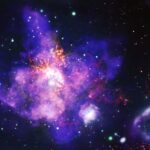 NASA’s Celestial Floral Arrangement An image of 30 Doradus, or the Tarantula Nebula, looks like a bouquet of purple flowers with orange stamens. Types of data are represented in different colors: X-ray data from NASA’s Chandra X-ray Observatory is blue and green, optical data from NASA’s Hubble Space Telescope is yellow, and radio data from the Atacama Large Millimeter/submillimeter Array is orange. There is a purple and green bubble-like shape at bottom right. This is a superbubble.