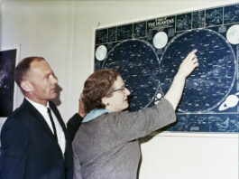 NASA Celebrates 100 Years Since Nancy Grace Roman’s Birth Two people - astronaut Buzz Aldrin and Dr. Nancy Grace Roman - look at a map of celestial objects hanging on a wall in front of them. The photos is taken from the side, so their profiles are visible. Aldrin wears a dark suit and tie, while Roman wears a gray short sleeved jacket. She is pointing at a constellation on the blue and white map.