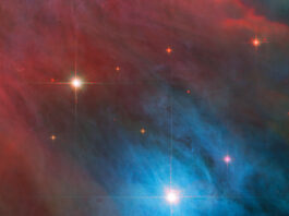 NASA’s Dynamic Duo: Stellar Achievements Unveiled Two stars with diffraction spikes shine brightly in the image. The larger star, at lower right, is in a bright blue cloud of gas and dust, while the smaller star at upper left is in a red haze. The clouds are somewhat patchy. Smaller red stars are scattered around them.