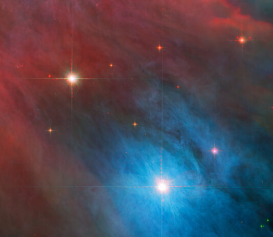 NASA’s Dynamic Duo: Stellar Achievements Unveiled Two stars with diffraction spikes shine brightly in the image. The larger star, at lower right, is in a bright blue cloud of gas and dust, while the smaller star at upper left is in a red haze. The clouds are somewhat patchy. Smaller red stars are scattered around them.