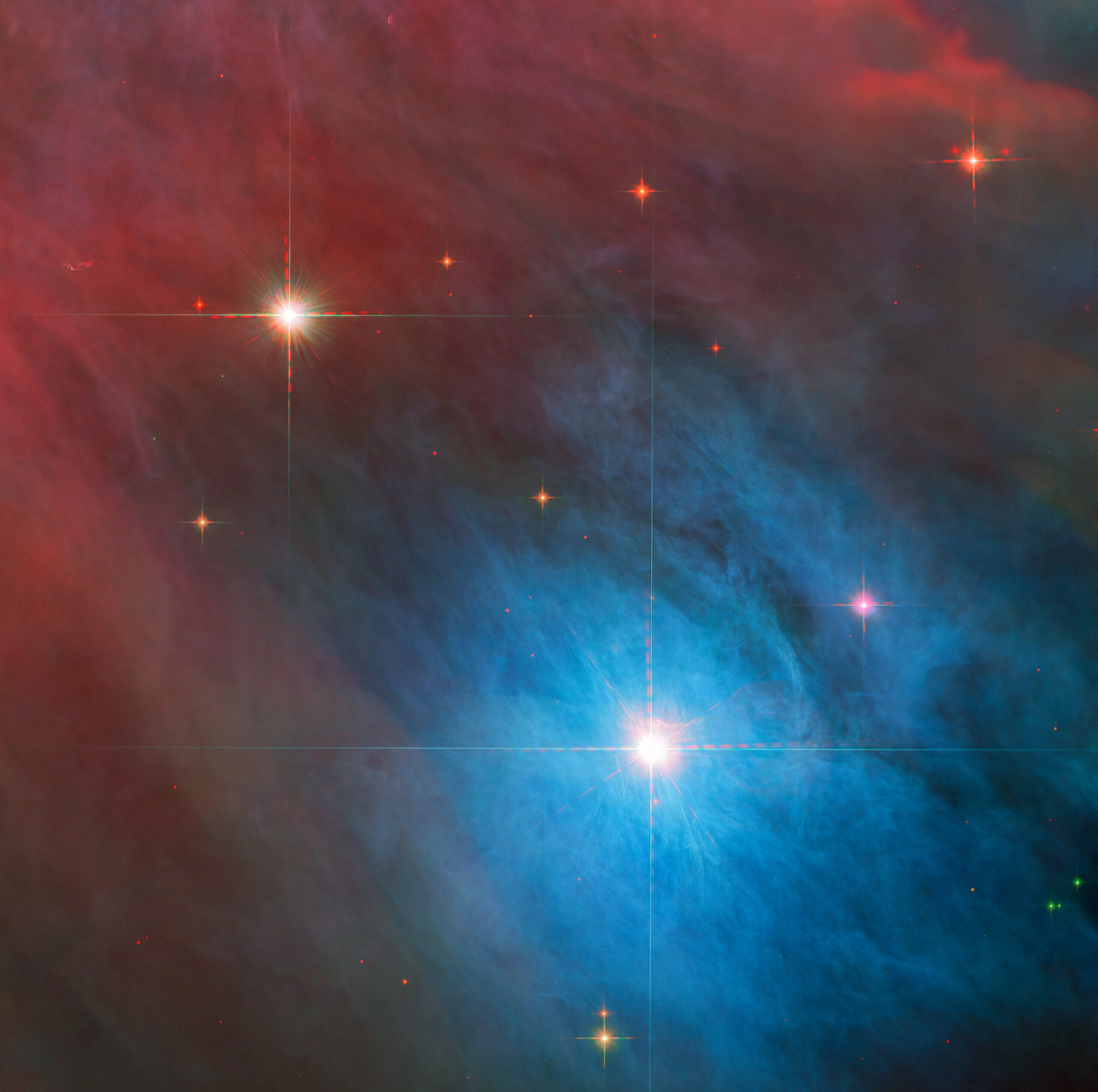 52689698469 aa39c2843b o.jpg Two stars with diffraction spikes shine brightly in the image. The larger star, at lower right, is in a bright blue cloud of gas and dust, while the smaller star at upper left is in a red haze. The clouds are somewhat patchy. Smaller red stars are scattered around them.