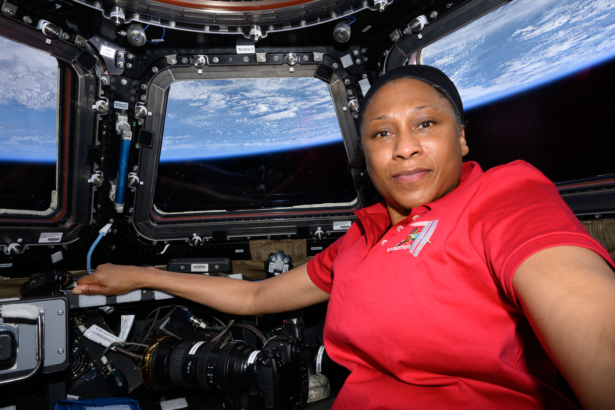53738633187 c3b7903f66 k.jpg A black woman in a red shirt poses in the International Space Station cupola with the Earth pictured behind her.