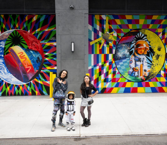 NASA Revives Art Program with NYC Mural in 2024 Two adults and a child pose for a photo in front of a colorful space-themed mural. The child wears an astronaut costume.