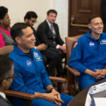 NASA Astronauts Rubio, Berrios Discuss Hispanic Heritage Month Two Hispanic men in blue jumpsuits with NASA patches on them sit at a table, smiling at people off screen. There are people of different ethnicities in the background.