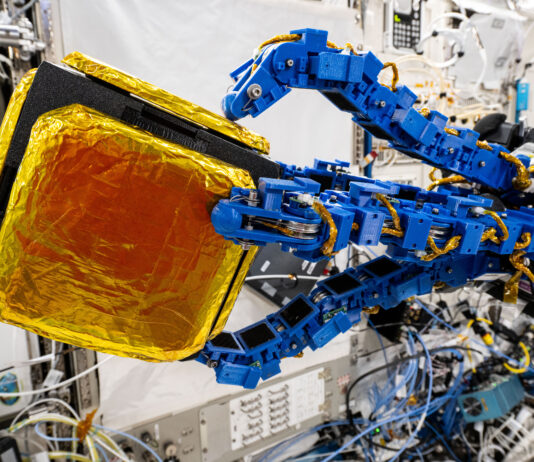 NASA’s Robot Achieves New Milestone in Dexterity Blue tentacle-like arms grip onto a black cube with gold foil patches on it.