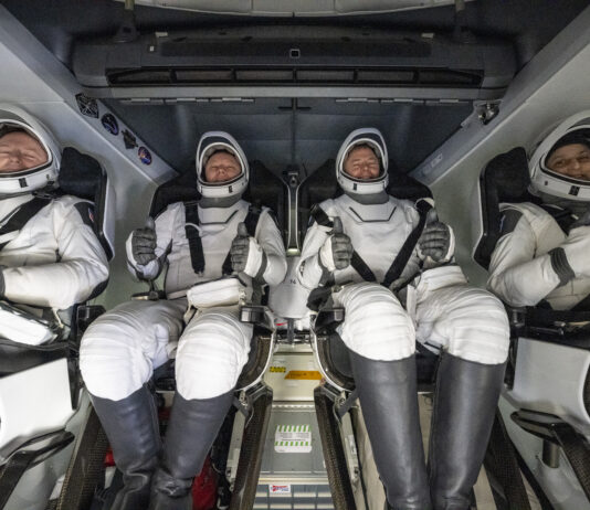 NASA Celebrates Crew-9’s Return Home Four people in white spacesuits, white helmets, and black boots give a thumbs up from inside a SpaceX Dragon spacecraft.