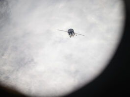 NASA Returns to Earth The Soyuz spacecraft looks like a cylinder with two lines stretching outward from it. It is oriented toward Earth, which is covered with white clouds.