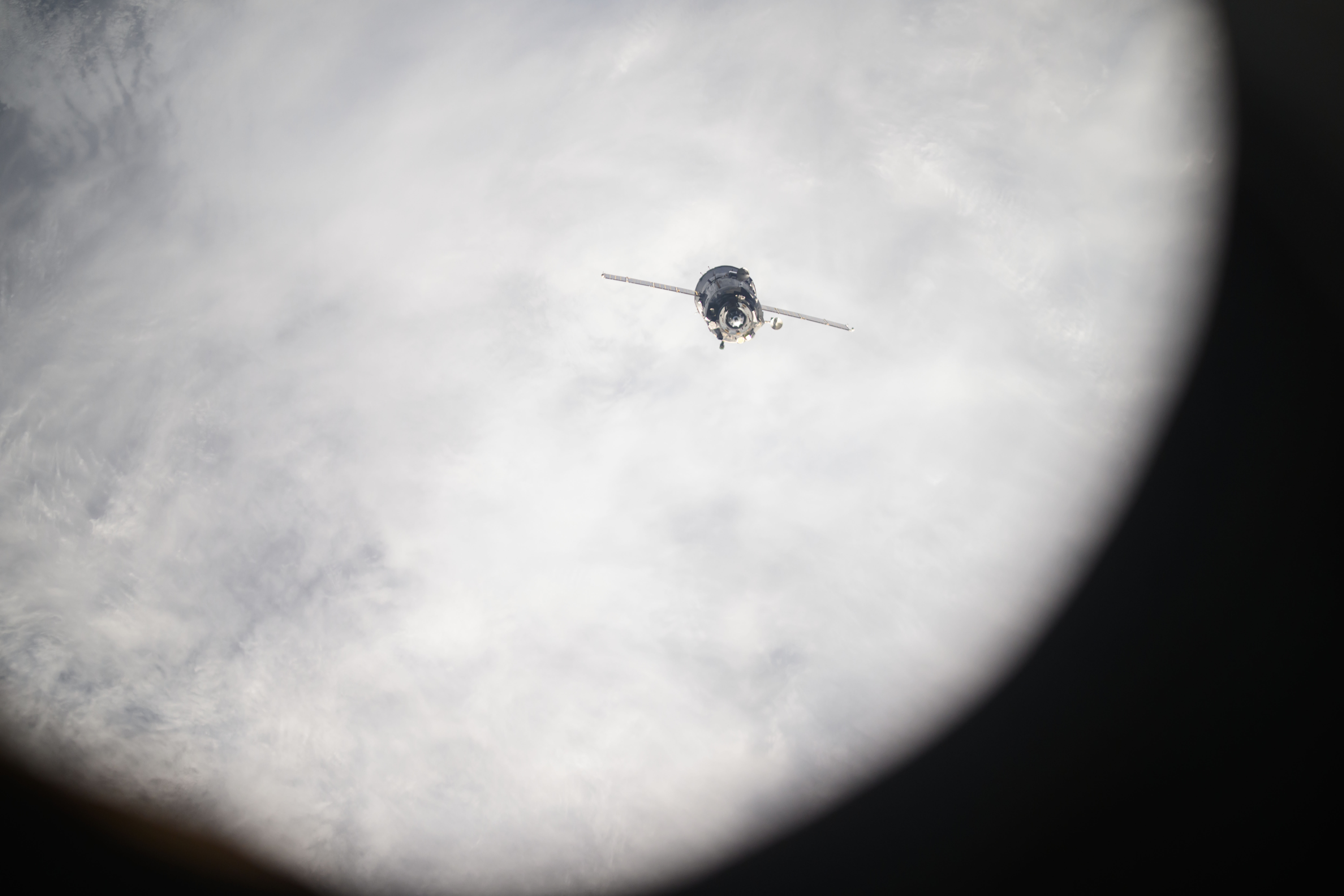 54470656907 2362dd2f92 o.jpg The Soyuz spacecraft looks like a cylinder with two lines stretching outward from it. It is oriented toward Earth, which is covered with white clouds.