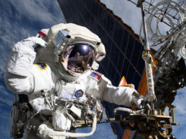 Anne McClain Conducts Research Aboard the Space Station An astronaut outside of the International Space Station has one hand on a truss near a solar panel. Her other hand is by her head. Reflected in her helmet is astronaut Nichole Ayers, also in a white spacesuit, taking the photo. Earth