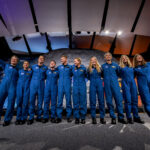New Group of Astronauts Selected by NASA Ten people in blue jumpsuits link arms. The two women on either end wave at the audience, who is not visible.