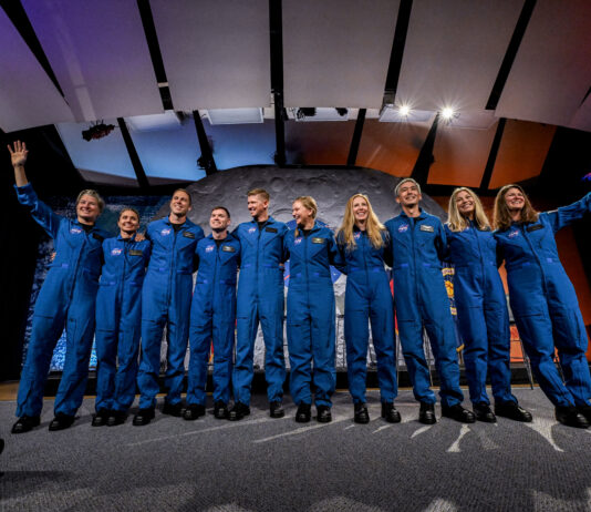 New Group of Astronauts Selected by NASA Ten people in blue jumpsuits link arms. The two women on either end wave at the audience, who is not visible.