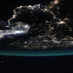 NASA Explores Urban Illuminations and Atmospheric Radiance Earth is a dark sphere with a glowing green border in this photo. We can only see one portion of it; in this photo’s orientation, we’re looking at the “bottom” of Earth’s sphere. City lights shine brightly at middle left; they are more dispersed throughout the rest of Earth that’s visible. Part of the space station is just barely visible at top left.