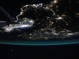 NASA Explores Urban Illuminations and Atmospheric Radiance Earth is a dark sphere with a glowing green border in this photo. We can only see one portion of it; in this photo’s orientation, we’re looking at the “bottom” of Earth’s sphere. City lights shine brightly at middle left; they are more dispersed throughout the rest of Earth that’s visible. Part of the space station is just barely visible at top left.
