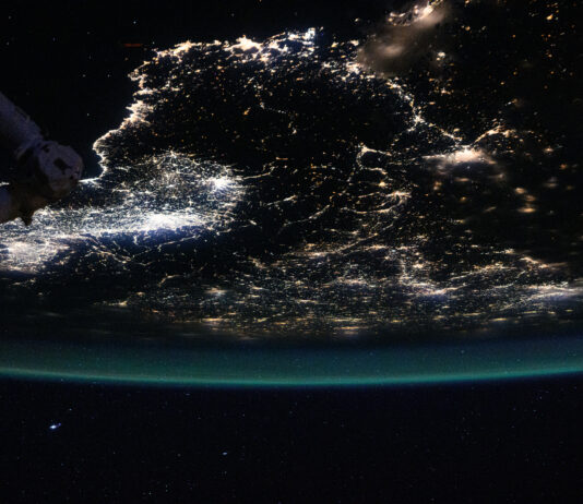 NASA Explores Urban Illuminations and Atmospheric Radiance Earth is a dark sphere with a glowing green border in this photo. We can only see one portion of it; in this photo’s orientation, we’re looking at the “bottom” of Earth’s sphere. City lights shine brightly at middle left; they are more dispersed throughout the rest of Earth that’s visible. Part of the space station is just barely visible at top left.