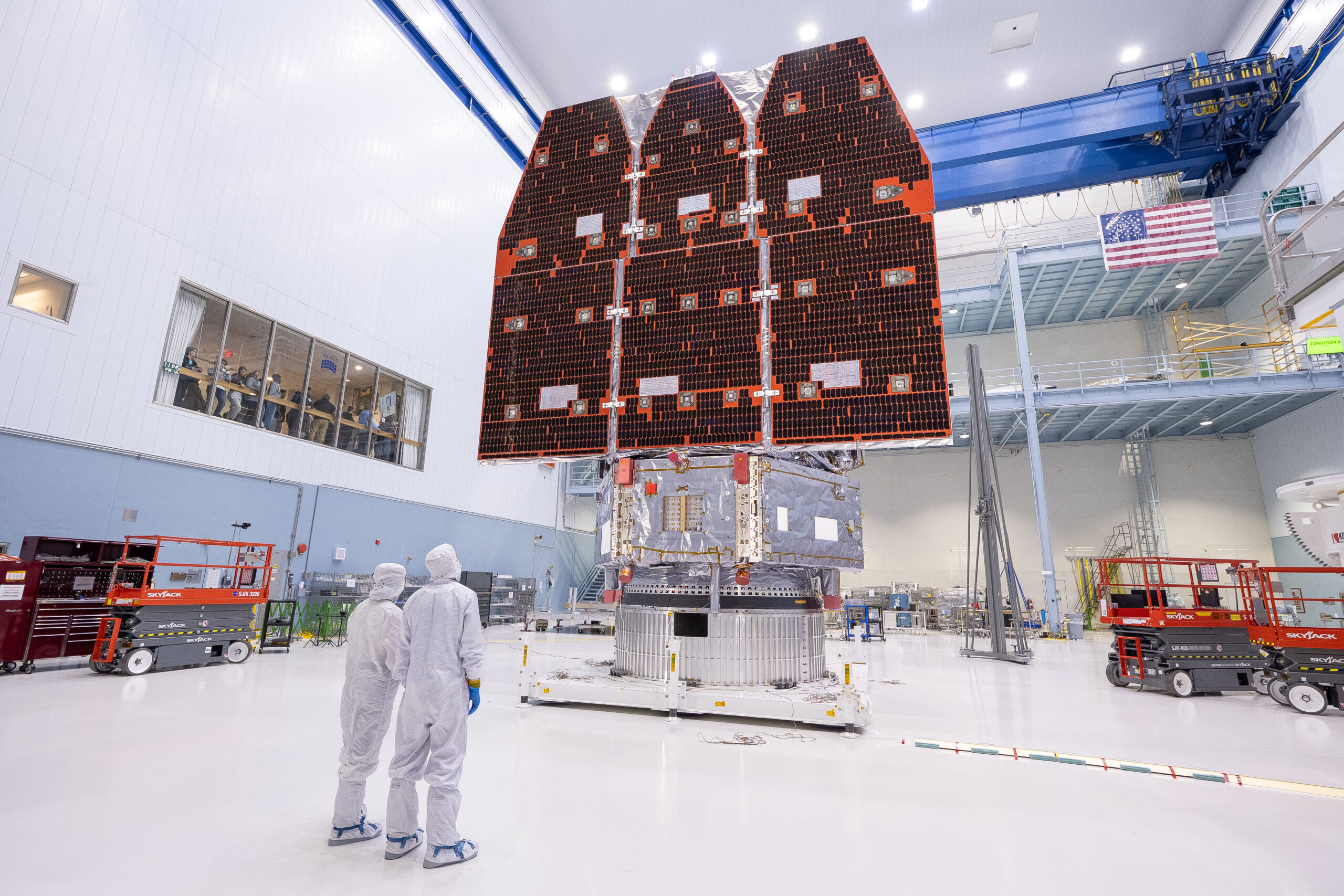54963276156 ab4f24f068 o.jpg Two people in white jumpsuits look up at a large telescope with three black and orange panels facing them. They are in a large white cleanroom with equipment and scaffolding.
