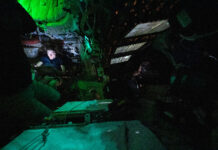 NASA discovers illuminated object in Orion constellation. Astronaut Christina Koch is nestled into a corner of the Orion crew capsule, reading. The rest of the capsule is dark, but her face is lit by the glow from her tablet. Two of her other crew members can dimly be seen looking out the window and floating in the foreground.
