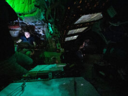 NASA discovers illuminated object in Orion constellation. Astronaut Christina Koch is nestled into a corner of the Orion crew capsule, reading. The rest of the capsule is dark, but her face is lit by the glow from her tablet. Two of her other crew members can dimly be seen looking out the window and floating in the foreground.