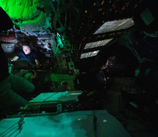 NASA discovers illuminated object in Orion constellation. Astronaut Christina Koch is nestled into a corner of the Orion crew capsule, reading. The rest of the capsule is dark, but her face is lit by the glow from her tablet. Two of her other crew members can dimly be seen looking out the window and floating in the foreground.