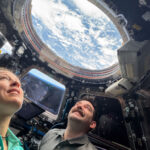 NASA Launches New Initiative to Explore the Night Sky Two astronauts look up through a round window in the International Space Station