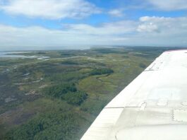 NASA Planes Conduct Science Missions for Air Quality Data The image shows an aerial view of the Chesapeake Bay, with groves of trees, rivers, a body of water in the distance, and green land. The horizon, a third of the way down the image, separates the blue cloudy sky from the land. On the right of the image is a white wing of a plane.