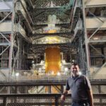 Aaron Rose Leads NASA’s Cold Stowage Mission at Station Nation A man poses in front of a large rocket inside of a facility.
