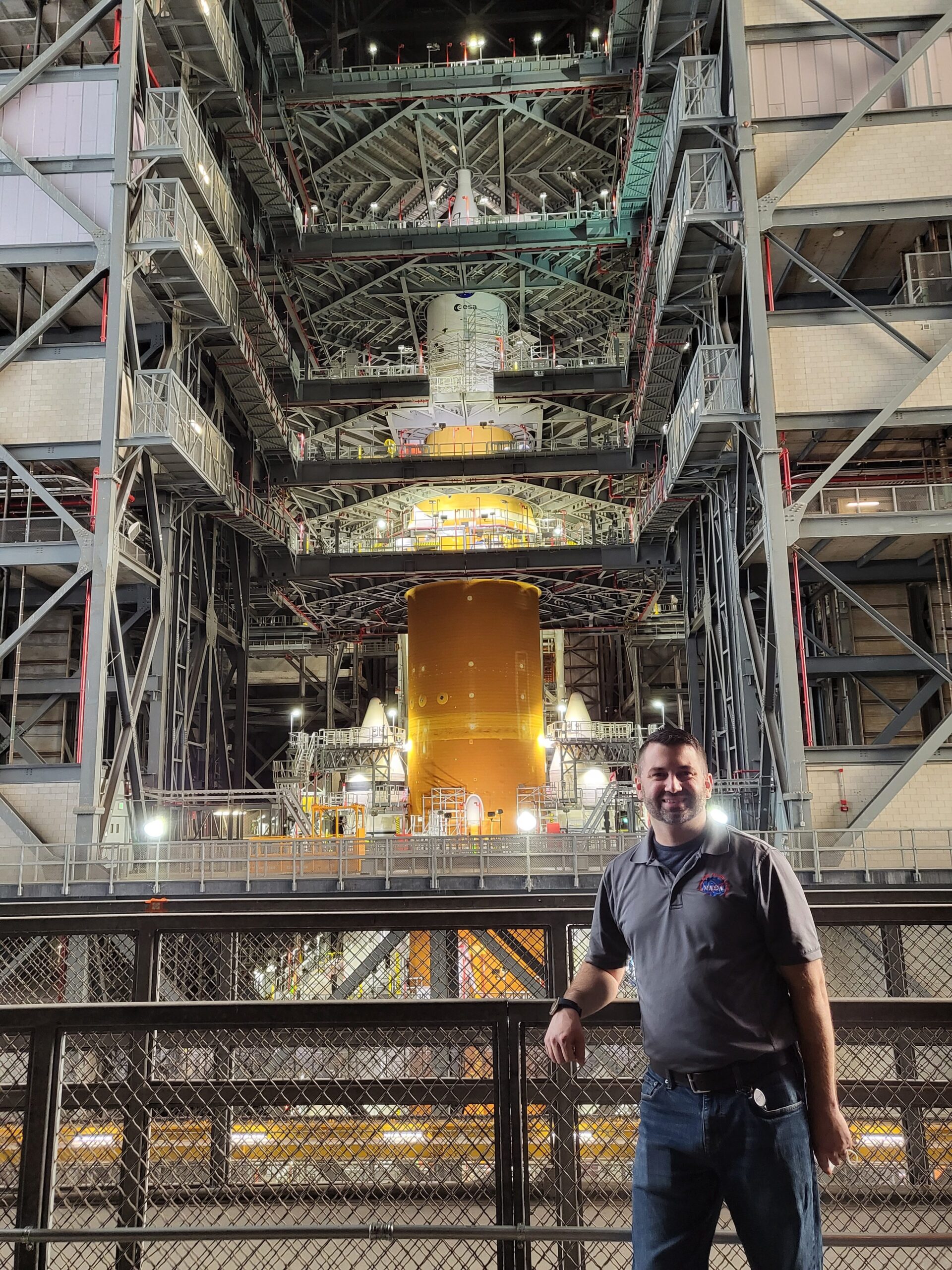 A man poses in front of a large rocket inside of a facility.