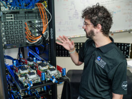 Understanding NASA’s Distributed Spacecraft Autonomy A man stands in front of a computer server and gestures towards the racks and cables.
