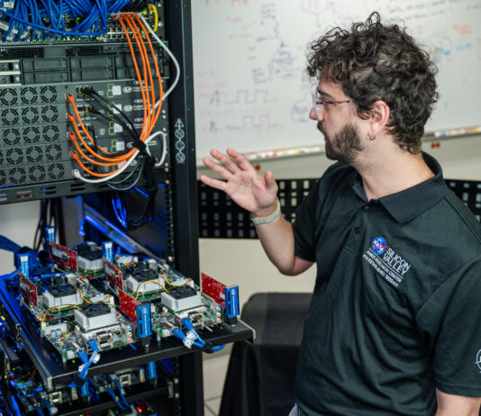 Understanding NASA’s Distributed Spacecraft Autonomy A man stands in front of a computer server and gestures towards the racks and cables.