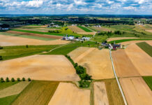 NASA-ISRO Collaboration to Track Crop Growth from Planting to Harvest Aerial view of Amish countryside with patchwork fields in shades of tan, green, and brown. White farmhouses and barns dot the landscape under a blue sky with fluffy white clouds.