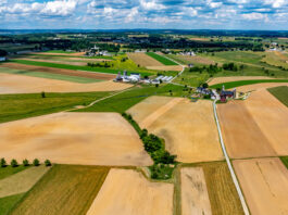 NASA-ISRO Collaboration to Track Crop Growth from Planting to Harvest Aerial view of Amish countryside with patchwork fields in shades of tan, green, and brown. White farmhouses and barns dot the landscape under a blue sky with fluffy white clouds.