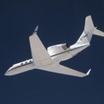 NASA Investigates Earth Science via Innovative Navigation System A white plane flies overhead against a dark blue sky. The plane is heading toward the left of the frame, and the NASA insignia is visible on its tail.