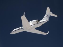 NASA Investigates Earth Science via Innovative Navigation System A white plane flies overhead against a dark blue sky. The plane is heading toward the left of the frame, and the NASA insignia is visible on its tail.
