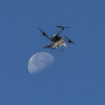 NASA Launches Atmospheric Research Probe A white, blue, and red probe attached to a rotor with four blades flies in the blue sky, just above the Moon.